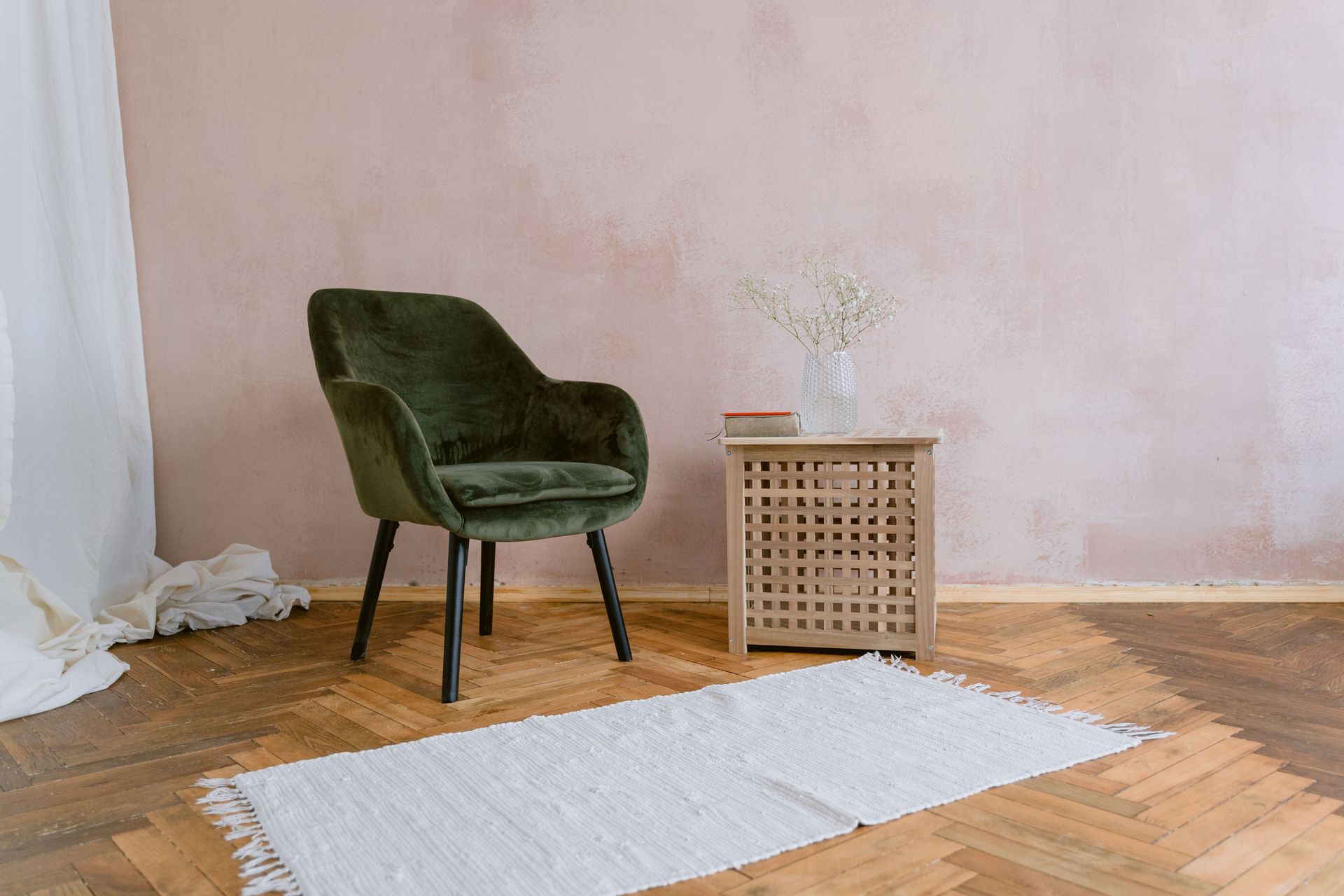 A minimalist room features a green chair, wooden side table, and a soft rug.